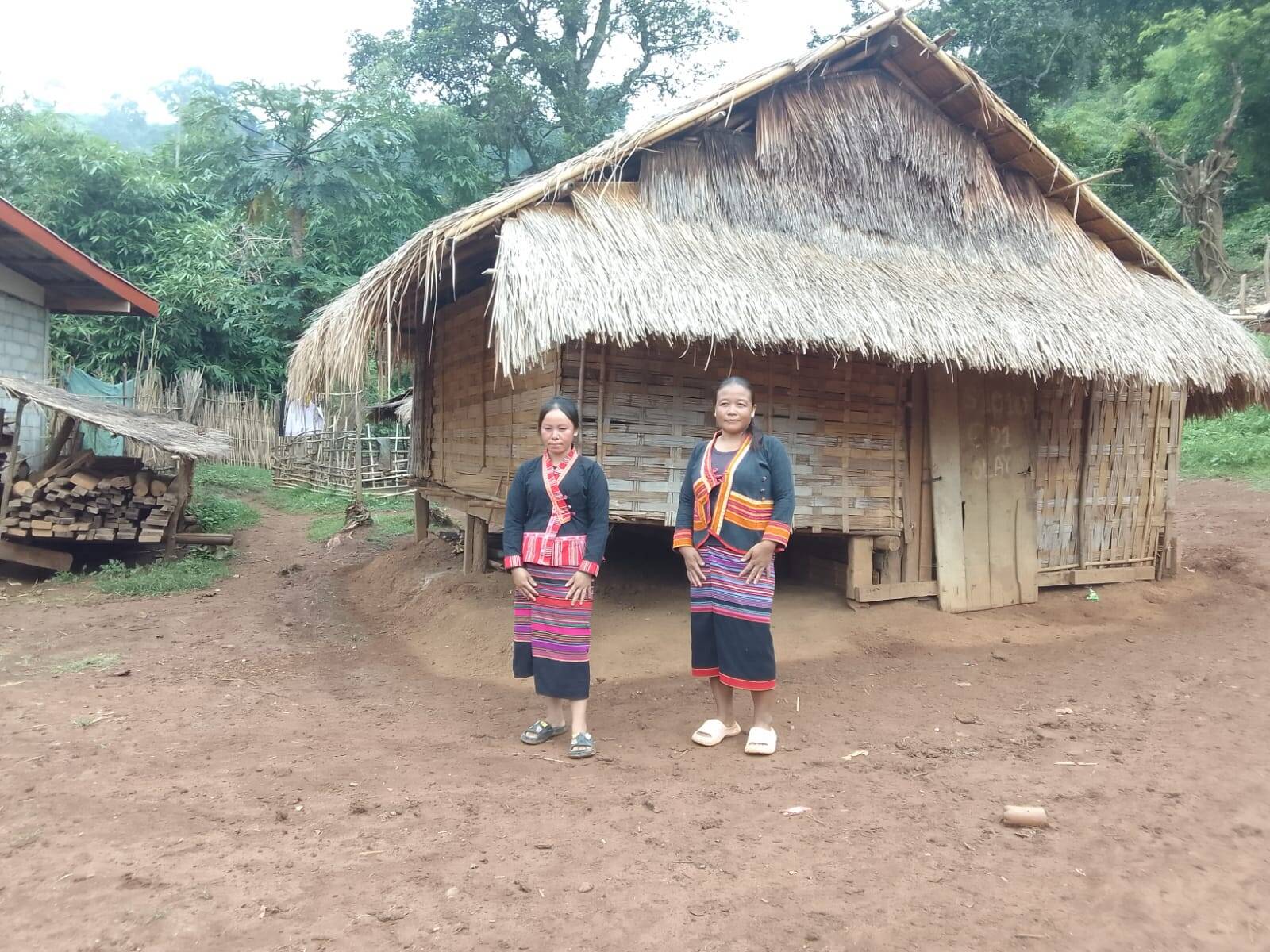 Two women in striped textile dress in front of a bamboo house
