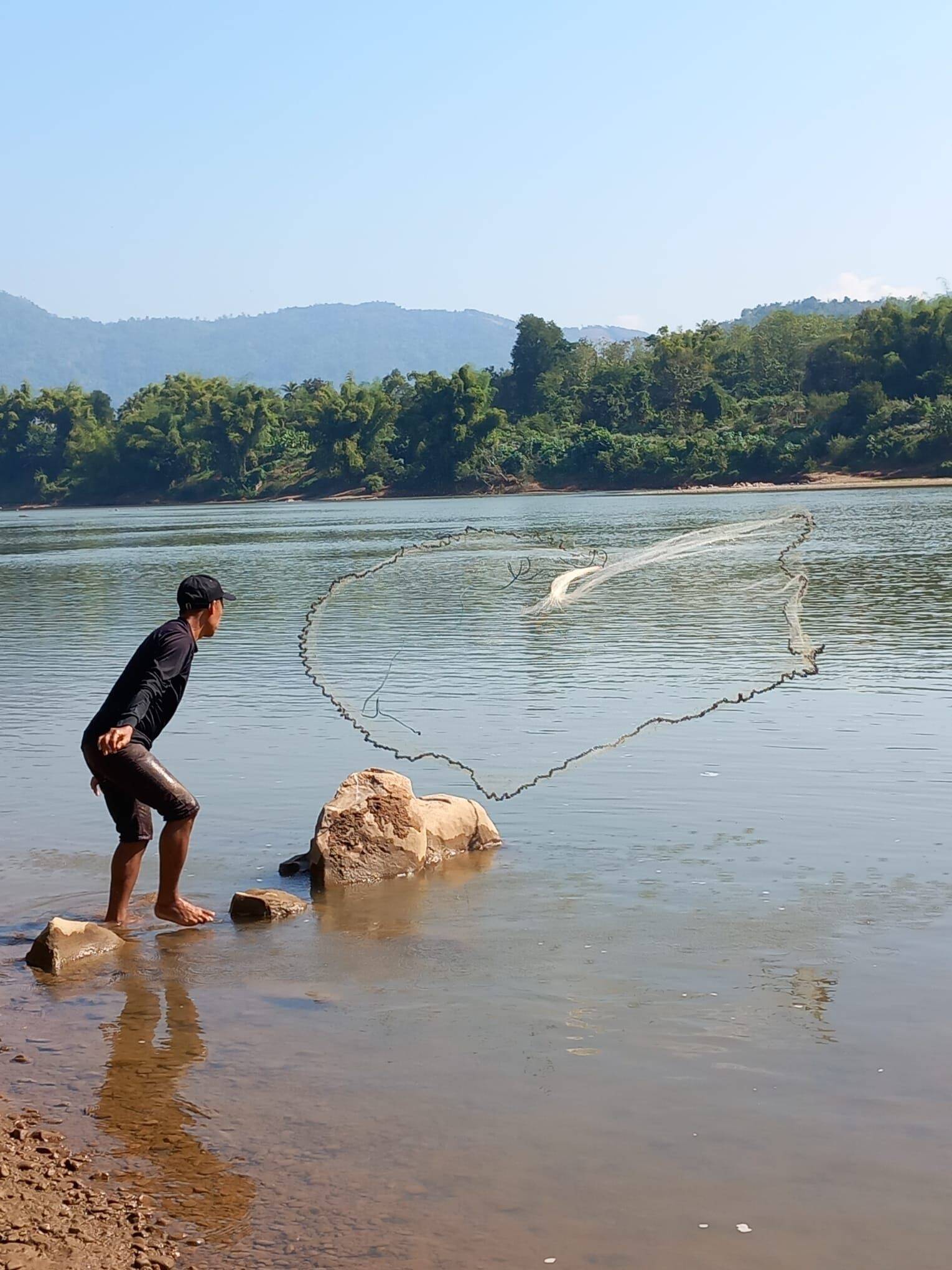 A man casting a fishing net from the riverbank