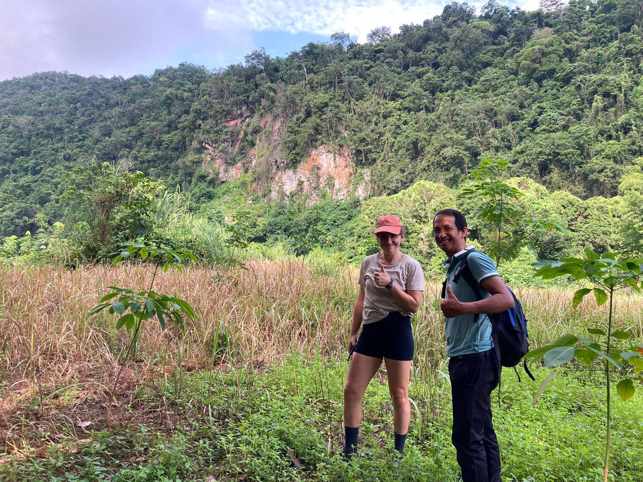 A guide and a guest on a trail below a forested cliff